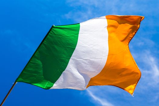 Irish flag fluttering in a brisk breeze against a bright blue sky. Europe.