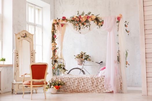 Rustic interior of the bedroom. A bed with an arch of flowers, a mirror, an armchair and a retro bicycle stands at the wall