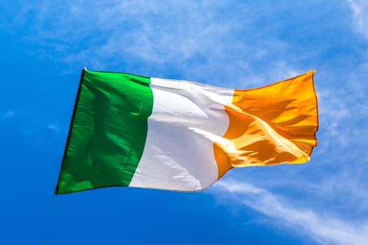 Irish flag fluttering in a brisk breeze against a bright blue sky. Europe.