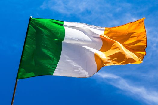 Irish flag fluttering in a brisk breeze against a bright blue sky. Europe.