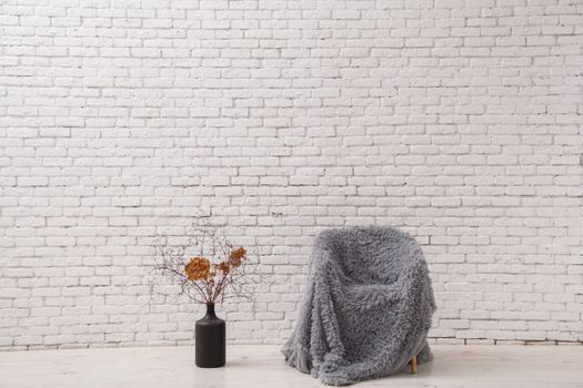 Interior in the style of minimalism. Chair and pot with dry branches against a white brick wall