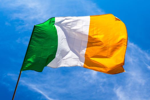 Irish flag fluttering in a brisk breeze against a bright blue sky. Europe.