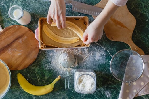 The girl puts the cut banana for the filling into the pie dough. Top view