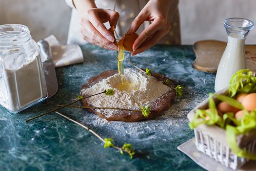 The baker pours the egg into the funnel in the flour on the table