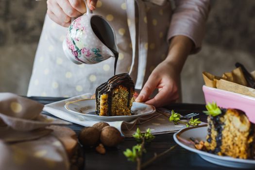 Close-up of the hand of baking girl is pouring chocolate glaze over a mouth-watering piece of cake