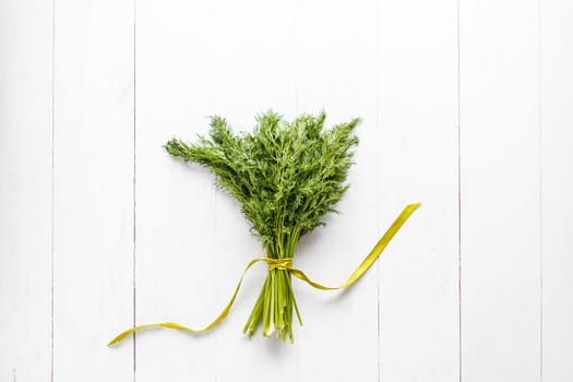 Bunch of fresh dill with ribbon on white wooden rustic background