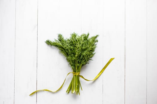 Bunch of fresh dill with ribbon on white wooden rustic background