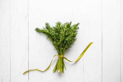 Bunch of fresh dill with ribbon on white wooden rustic background
