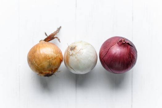 Three bulbs on a white wooden background. White onions, onions and red onions. Top view