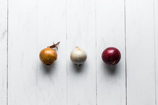 Three bulbs on a white wooden background. White onions, onions and red onions. Top view