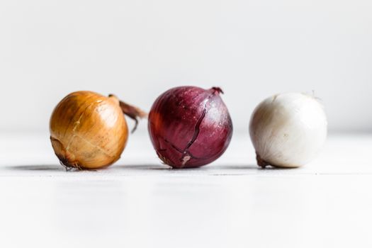 Three bulbs on a white wooden background. White onions, onions and red onions.