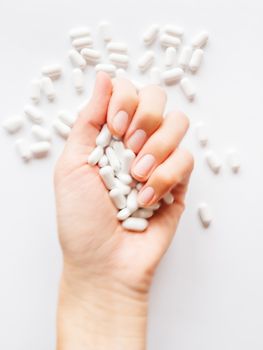 Palm hand full of white scattering pills. Woman gripes hand with capsules with medicines on light background. Flat lay, top view.