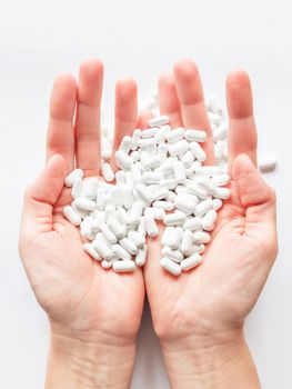 Palm hands full of white scattering pills. Woman gripes hand with capsules with medicines on light background. Flat lay, top view.