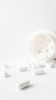 White pills spilled out of a plastic jar. Medicine capsules on white background with copy space.