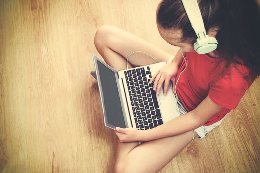 High angel view of a girl sitting on the floor and listening to music on her laptop (vintage effect).