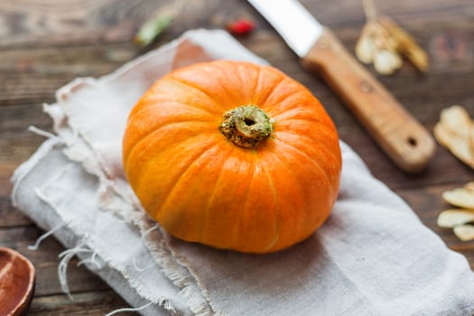 Fresh orange pumpkin on wooden table. Homespun napkin and rustic cutlery on background.