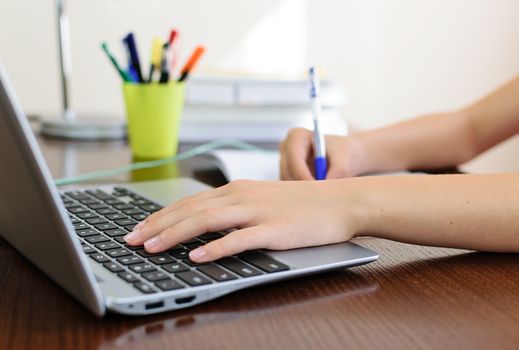 Young female student doing homework on a desk with a laptop.