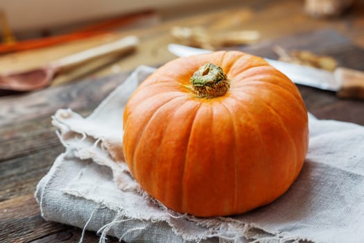 Fresh orange pumpkin on wooden table. Homespun napkin and rustic cutlery on background.