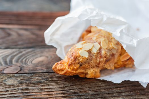 Tasty croissant in white paper bag on table. Rustic wooden background with sweet dessert.