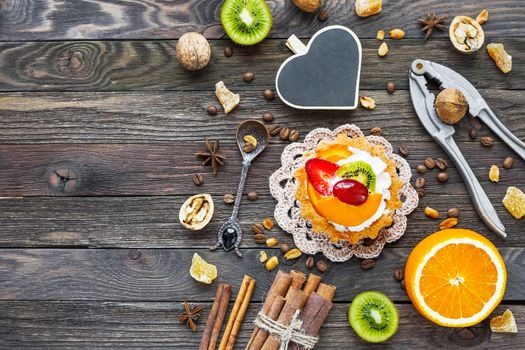 Rustic wooden background with fruit tart, spices, kiwi and oranges. Heart chalkboard for text.Top view, flat lay.