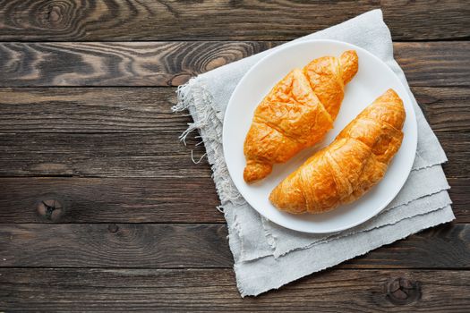 Continental breakfast background - pair of croissants on homespun napkin. Rustic wooden background with place for text. Top view.