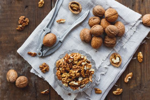 Glass bowl with walnuts on rustic homespun napkin. Healthy snack on old wooden background.