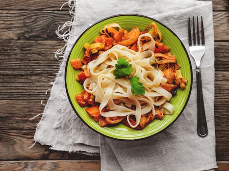 Green plate with tasty fettuccine and tomato sauce. Top view on wooden table, napkin and bowl with pasta. Italian cuisine.