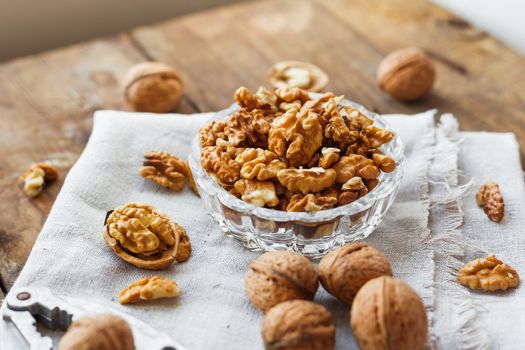 Glass bowl with walnuts on rustic homespun napkin. Healthy snack on old wooden background.