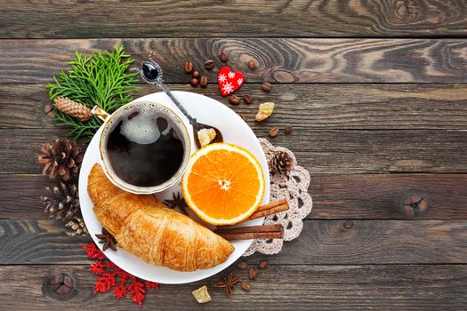 Christmas and New Year background with continental breakfast - cup of hot coffee with cinnamon, fresh orange and croissant. Decorations - snowflake, crochet napkin, pine cones.