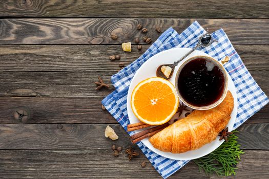 Continental breakfast - cup of hot coffee, croissant and orange. Tasty food on plaid blue napkin. Rustic wooden background. Top view, place for text.