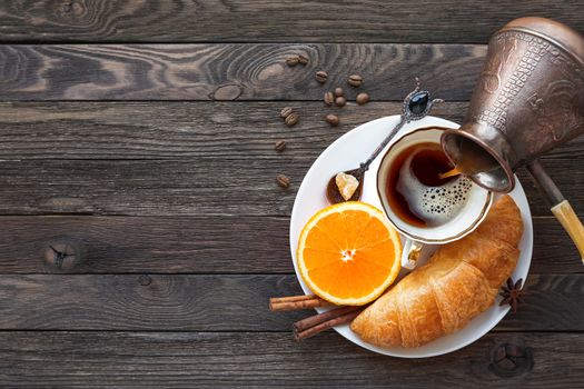 Continental breakfast - cezve and cup of hot coffee, croissant and orange. Tasty food on rustic wooden background. Top view, place for text.
