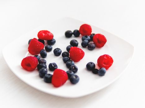Fresh blueberries and raspberries white plate. Light and cozyozy background with healthy food. Fresh-gathered berries full of vitamins, good for diet nutrition and healthy meals.