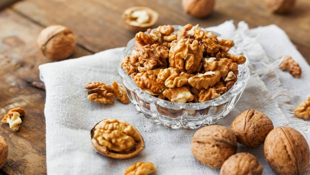 Glass bowl with walnuts on rustic homespun napkin. Healthy snack on old wooden background.