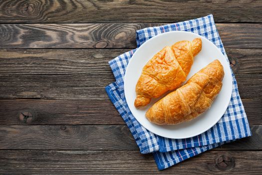 Continental breakfast background - pair of croissants on plaid blue napkin. Rustic wooden background with place for text. Top view.