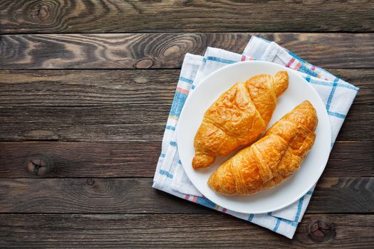 Continental breakfast background - pair of croissants on plaid blue napkin. Rustic wooden background with place for text. Top view.