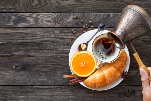 Continental breakfast - cezve and cup of hot coffee, croissant and orange. Tasty food on rustic wooden background. Top view, place for text.