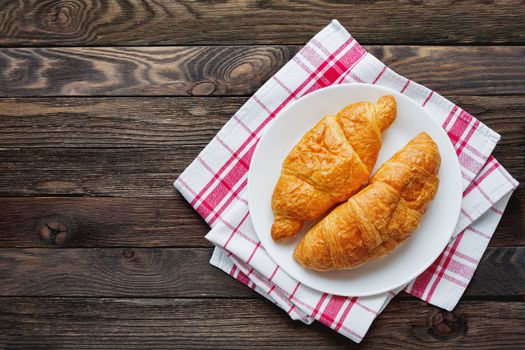 Continental breakfast background - pair of croissants on plaid red napkin. Rustic wooden background with place for text. Top view.