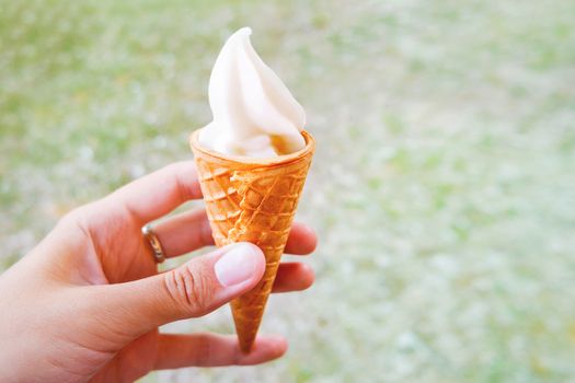 Woman holds an ice cream cone. Frozen creamy dessert in waffle cone. Place for text.
