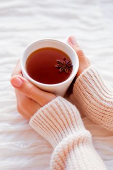 Women holds a cup of hot tea with anise star. Cozy morning at home.