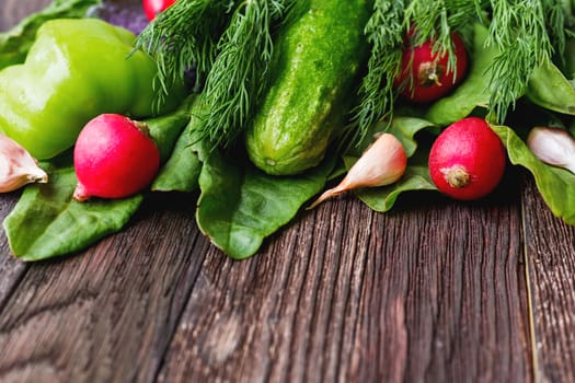 Fresh ingredients for salad - sorrel leaves, radishes, cucumber, sweet pepper, garlic, dill on wooden background. Rustic table with tasty vegetables. Place for text.