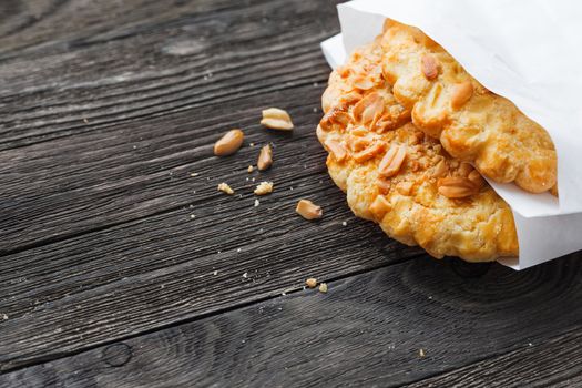 Tasty tart with peanuts in white paper bag. Rustic wooden background with sweet dessert. Place for text.
