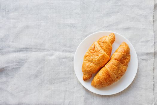 Continental breakfast background - pair of croissants on homespun napkin. Rustic wooden background with place for text. Top view.