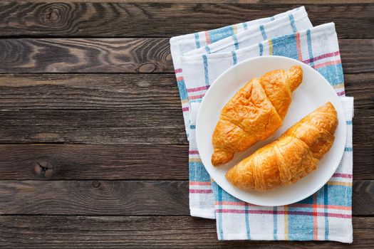 Continental breakfast background - pair of croissants on plaid blue napkin. Rustic wooden background with place for text. Top view.