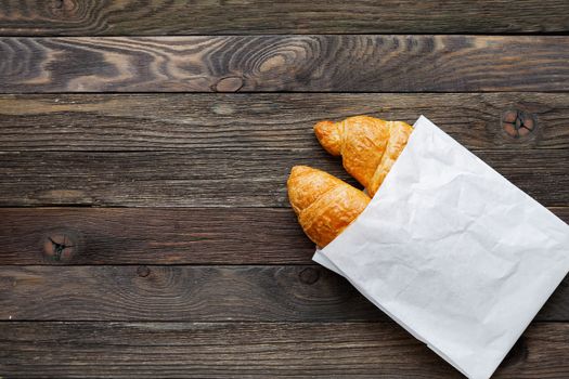 Tasty croissants in white paper bag. Rustic wooden background with sweet dessert. Top view.