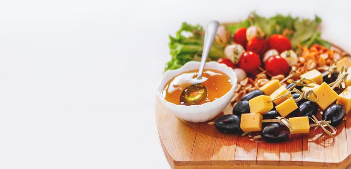 Wooden cutting board with snacks - honey, olives with cheese, vegetables. White copy space.