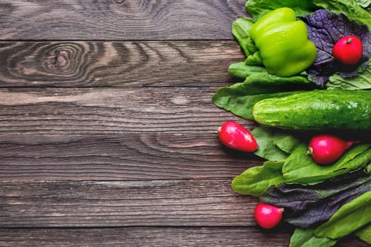 Fresh ingredients for salad - sorrel leaves, radishes, cucumber, sweet pepper on wooden background. Rustic table with tasty vegetables. Place for text.