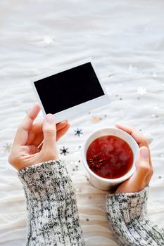 Woman holds a cup of tea and photo. Winter fabric background with sparkling silver snowflakes. Empty photo frame for your text or picture.