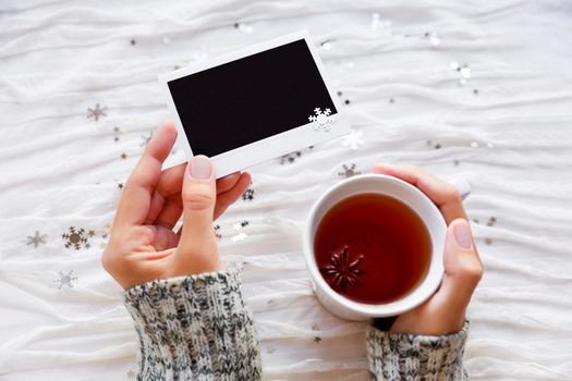 Woman holds a cup of tea and photo. Winter fabric background with sparkling silver snowflakes. Empty photo frame for your text or picture.