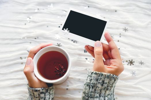 Woman holds a cup of tea and photo. Winter fabric background with sparkling silver snowflakes. Empty photo frame for your text or picture.