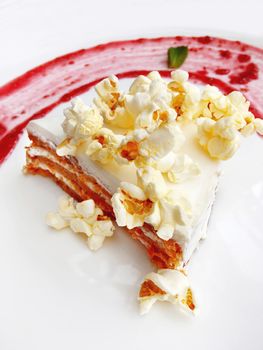 Carrot cake with popcorn sprinkles and raspberry jam. Tasty dessert on white plate.